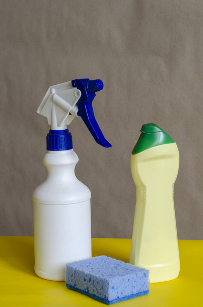 Plastikflaschen mit Reinigungsprodukten und Schwamm auf zweifarbigem Hintergrund. Verschiedene Behälter für Haushaltschemikalien. Reinigungsunternehmen oder Produkte. Seitenansicht. Nahaufnahme. - Foto, Bild