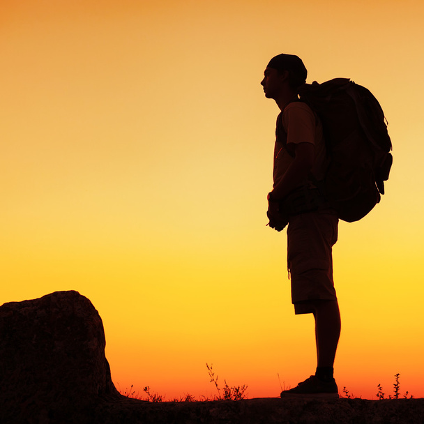 Турист с рюкзаком стоит на вершине горы и наслаждается
 - Фото, изображение