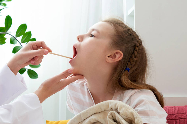 Médecin des enfants examinant les petites filles gorge à la maison avec un dépresseur de langue
 - Photo, image