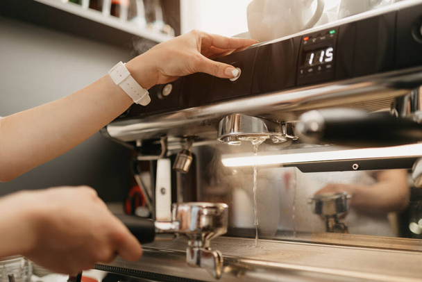 A female barista purging a grouphead thoroughly with hot water in the espresso machine in a coffee shop. A barista cleaning in a cafe. - Photo, Image