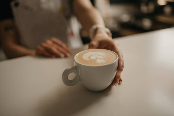 Kobieta barista trzyma filiżankę gorącej latte dla klienta w kawiarni. Kelnerka przygotowująca zamówienie klienta - Zdjęcie, obraz