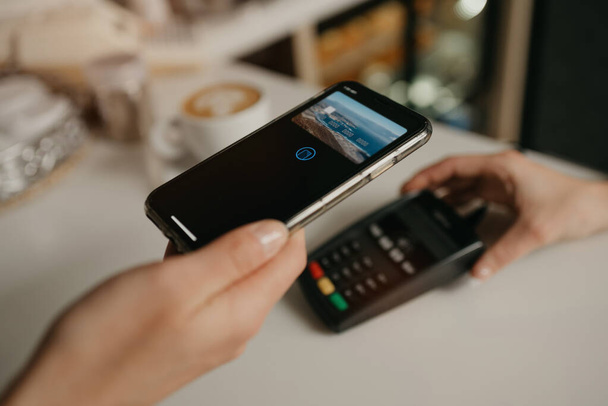 Eine Dame bezahlt ihren Latte in einem Café mit dem Smartphone per kontaktloser PayPASS-Technologie. Eine Barista hält einem Kunden in einem Coffeeshop ein Terminal zur Bezahlung hin. - Foto, Bild