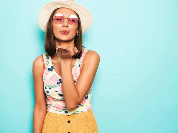 Young beautiful woman looking at camera in hat.Trendy girl in casual summer white T-shirt and yellow skirt in round sunglasses. Positive female shows facial emotions. Gives air kiss - Photo, Image