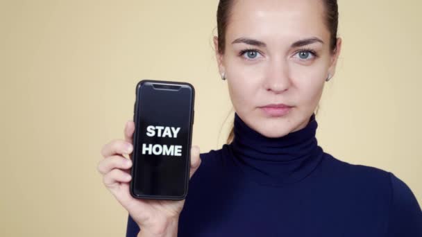 Retrato de chica morena muestra teléfono con inscripción permanecer en casa durante la epidemia
 - Metraje, vídeo