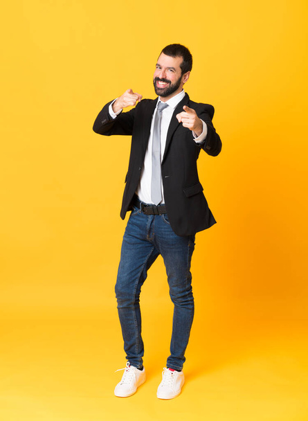 Full-length shot of business man over isolated yellow background points finger at you while smiling - Foto, Imagem