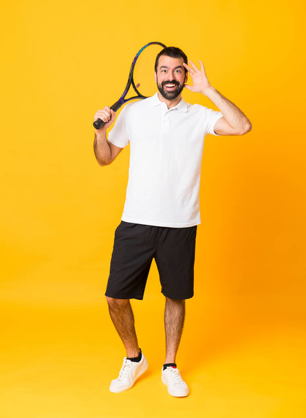 İzole edilmiş sarı arka planda tenis oynayan bir adamın tam boy çekimi. - Fotoğraf, Görsel