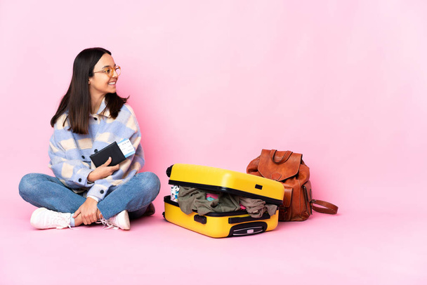Mujer viajera con una maleta sentada en el suelo mirando hacia un lado
 - Foto, imagen