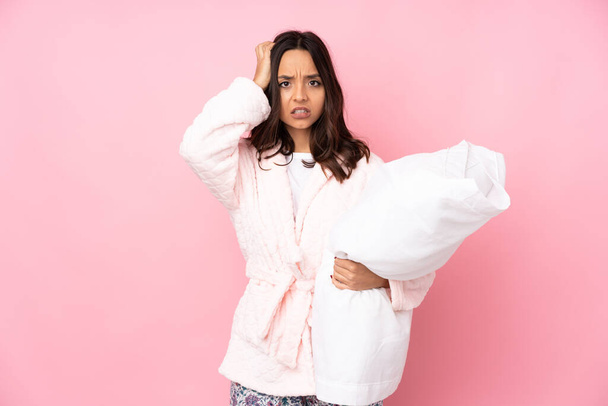 Young woman in pajamas isolated on pink background having doubts - Foto, imagen