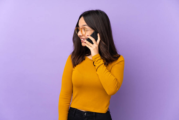紫色の背景に隔離された若い混合人種の女性は誰かと携帯電話との会話を保ちます - 写真・画像