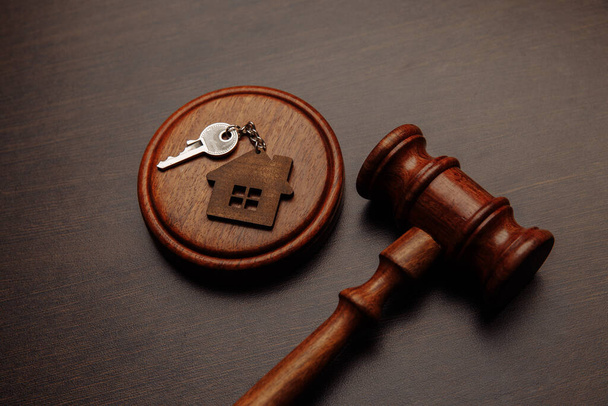 Judge gavel and key chain in shape of two splitted part of house on wooden background. Concept of real estate auction or dividing house when divorce, division of property, real estate, law system - Photo, Image