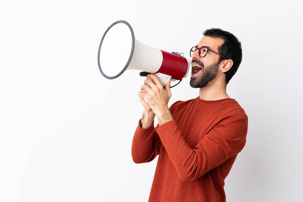 Caucasian handsome man with beard over isolated white background shouting through a megaphone - Φωτογραφία, εικόνα