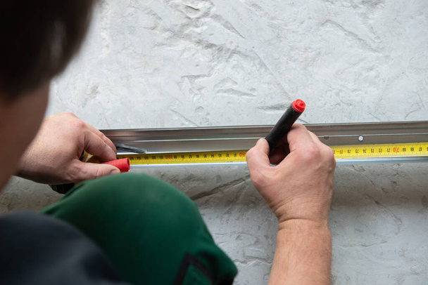 Male worker works with profile for drywall, marker marks for cutting. Construction work, repair. Renovation - Φωτογραφία, εικόνα