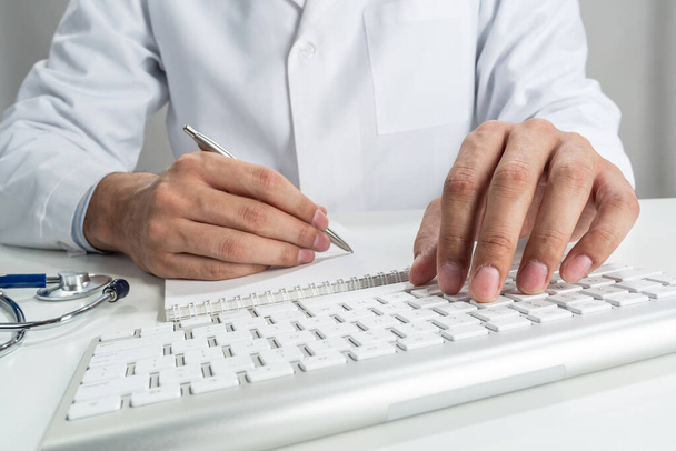 Doctor typing on wireless computer keyboard in office. Physician in white medical gown works with computer at desk. Professional diagnosis and treatment in modern hospital. Professional healthcare - Фото, зображення
