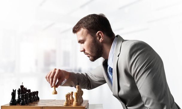 Businessman moving chess figure in chessboard. Successful management and leadership concept. Handsome man in business suit sitting at desk with chess. Operative tactics and strategy planning - Fotografie, Obrázek