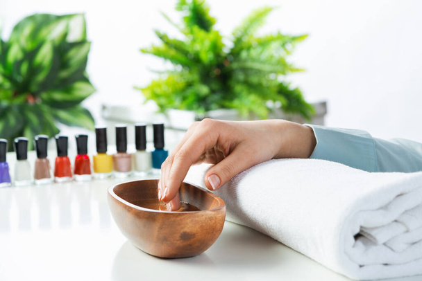 Closeup female hand in wooden bowl with water. Spa procedure and relaxation. Female hand preparing for manicure. Professional nail care and beautician service. Beauty and hygiene concept - Foto, Imagem
