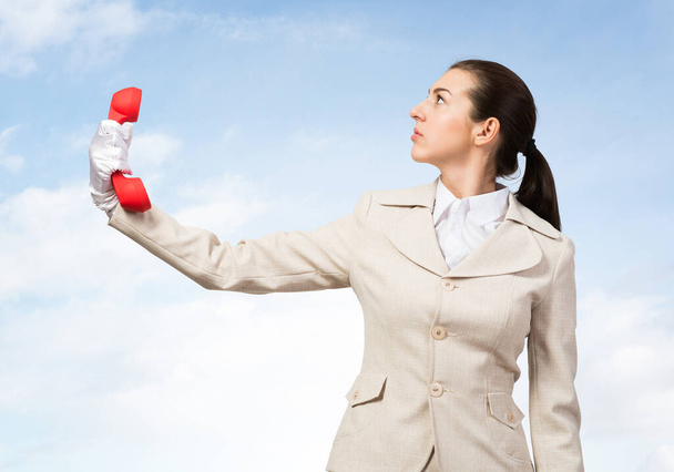 Businesswoman holds vintage red phone on distance. Telemarketer in business suit with telephone looks upward on blue sky background. Employee ignores communication. Business assistance and support - Photo, image