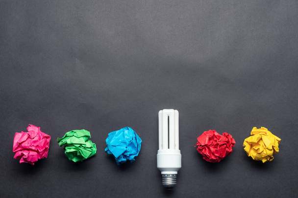 Fluorescent lamp and crumpled colorful paper balls on black background. Successful solution of problem. Idea generation and brainstorming motivation. Great idea among failing ideas metaphor. - Photo, Image