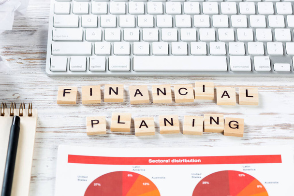 Financial planning concept with letters on cubes. Still life of office workplace. Flat lay vintage wooden desk with computer keyboard and analytic report. Company development and consulting analysis. - 写真・画像