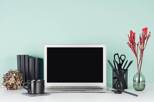 Workspace with blank laptop monitor, black stationery, books, round sheaf of dry brown branches, coffee cup, red plant in  green mint menthe interior on white wood desk. - Photo, Image