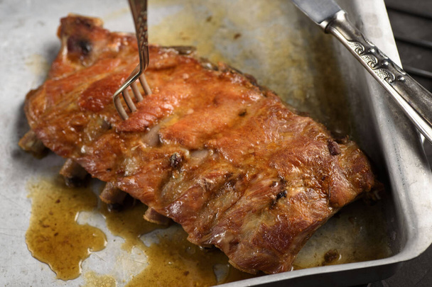 Roast pork rib on a baking sheet and with a fork stuck - Photo, Image