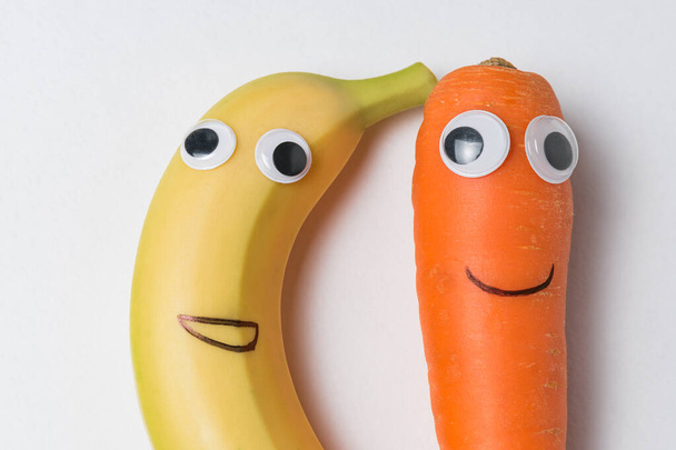 Banan i marchewka z googlowymi oczami i malowanymi uśmiechami. Produkty o śmiesznych twarzach - Zdjęcie, obraz
