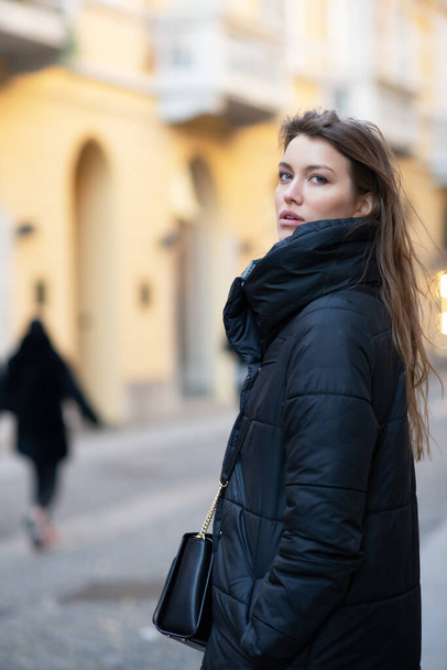 Young caucasian woman dressed in black clothes. Beautiful caucasian girl posing outdoor in Milan, Italy. Street fashion, winter outdoor - Foto, Bild