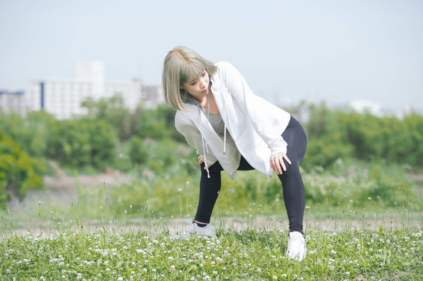 Ασιάτισσα νεαρή γυναίκα κάνει διατάσεις άσκηση σε αστικό πράσινο χώρο - Φωτογραφία, εικόνα
