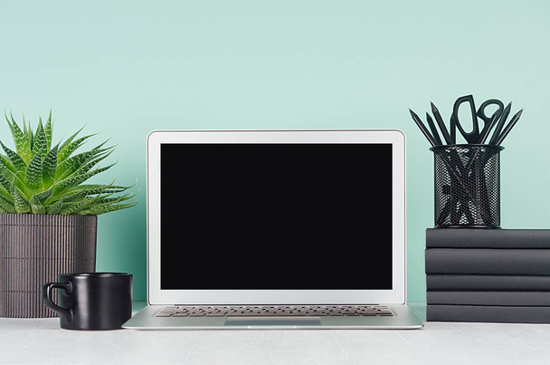 Fresh home workspace with blank laptop monitor, black stationery, books, coffee cup, aloe house plant in elegant green mint menthe interior on white wood desk. - Photo, image