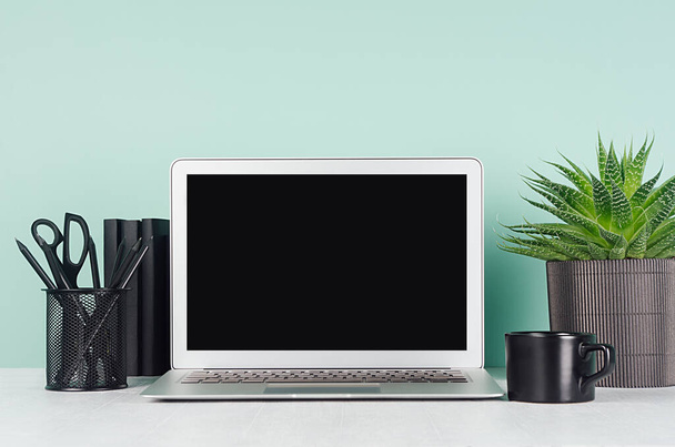 Spring workplace with blank notebook screen, black stationery, books, aloe plant in ribbed pot, coffee cup, in elegant green mint menthe interior on white wood table. - Photo, image