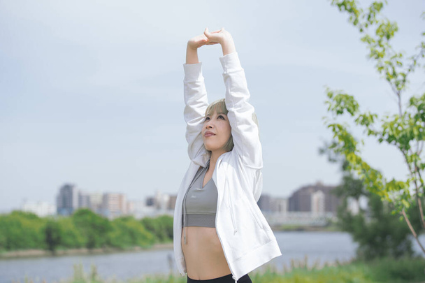 Asiatische junge Frau bei Stretching-Übungen im städtischen Grünraum - Foto, Bild