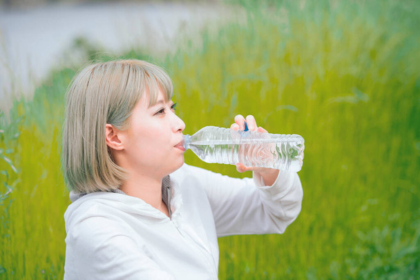 Asiática joven hidratante durante el ejercicio en el espacio verde urbano
 - Foto, Imagen