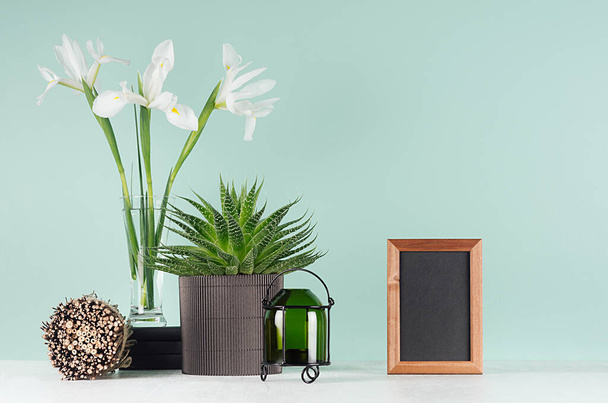Elegant spring interior with white flowers, black books, blank photo frame, green aloe, candlestick, round sheaf of twigs on green mint menthe wall and white wood table. - Photo, image