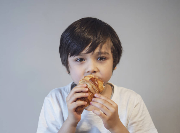 Kind jongen croissant voor zijn ontbijt voordat ga naar school in de ochtend, Gezond eten voor kind concept - Foto, afbeelding