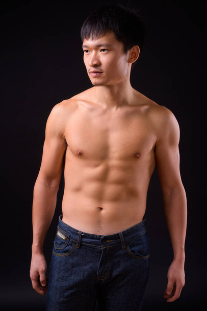 Studio shot of young muscular Chinese man shirtless against black background - Foto, afbeelding