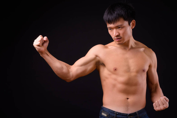 Studio shot of young muscular Chinese man shirtless against black background - Foto, afbeelding