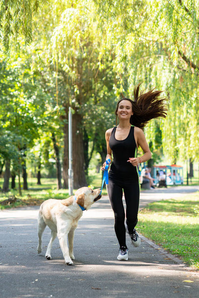 Cheerful pretty young woman walking and running with her dog in summer park. Active leisure, beautiful brunette girl at morning  jogging with puppy - Fotoğraf, Görsel
