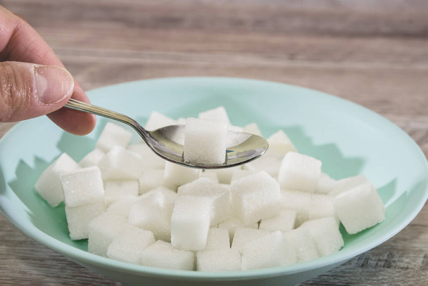 cubes de sucre dans une assiette et une cuillère sur un fond en bois. Le concept du mal de sucre. Mangez du sucre avec une cuillère
. - Photo, image