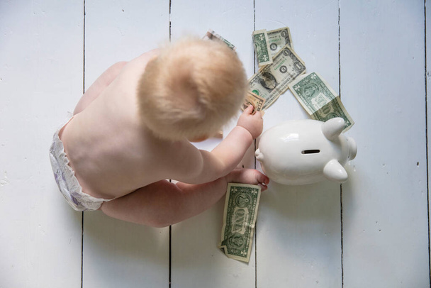 Young baby sitting on the floor putting money into a piggy bank money box - Zdjęcie, obraz