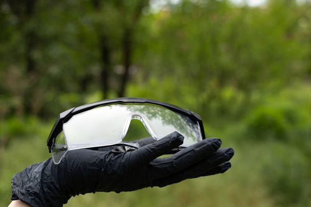 рука в чорних медичних рукавичках тримає медичні окуляри на ізольованому фоні
 - Фото, зображення