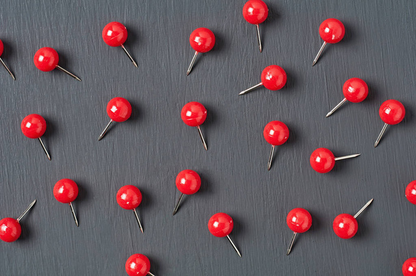 Scattered many red push pins on dark concrete desk in office, school or home. Close-up - 写真・画像