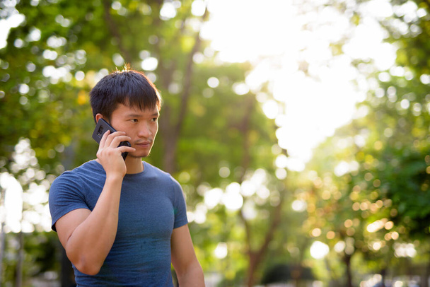 Portrait of young Asian man talking on the phone at the park outdoors - Фото, изображение