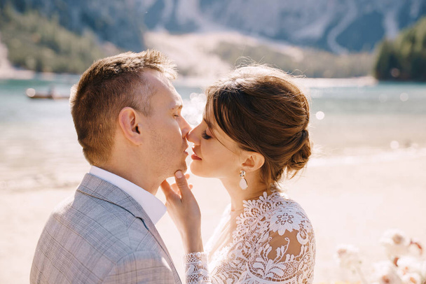 Los recién casados se besan en el lugar de la ceremonia, con un arco de columnas de flores de otoño, sobre el telón de fondo del Lago di Braies en Italia. Boda de destino en Europa, en el lago Braies
. - Foto, imagen