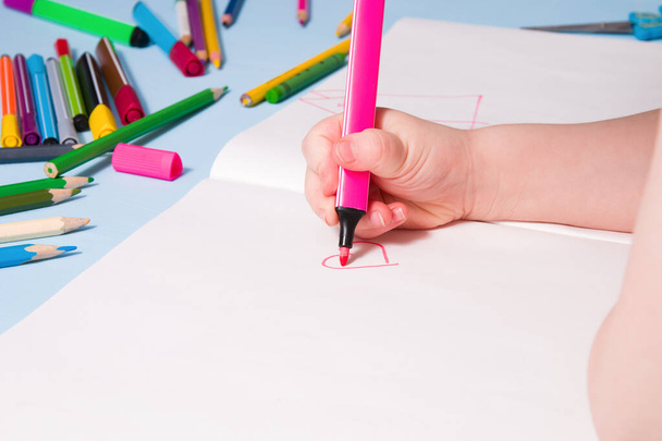 a small child draws with a pink felt-tip pen a heart in an album, copy space, top view, blue background, what to do with a quarantined child, activities for children at home - Fotó, kép