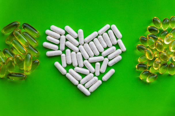 Forme de coeur de suppléments vitaminiques blancs avec pile de pilules de gelée jaune, gélule diététique santé aimante sur fond vert vif avec espace de copie - Photo, image