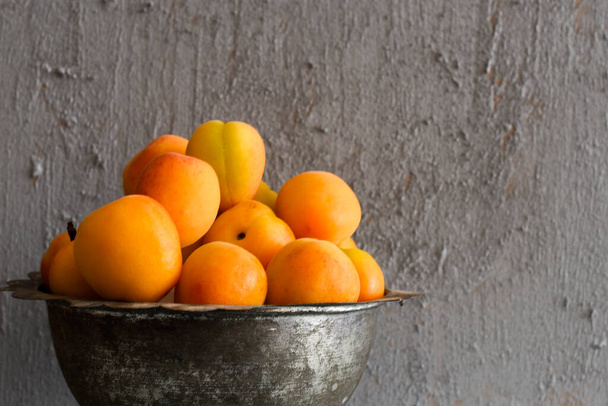 Apricots in a Vintage Bowl with Cinnamon Sticks and Leaves on a Grey Concrete Background - Fotó, kép
