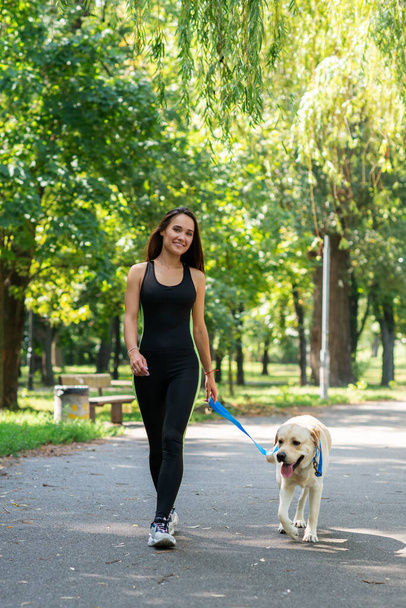 Cheerful pretty young woman walking and running with her dog in summer park. Active leisure, beautiful brunette girl at morning  jogging with puppy - Fotoğraf, Görsel
