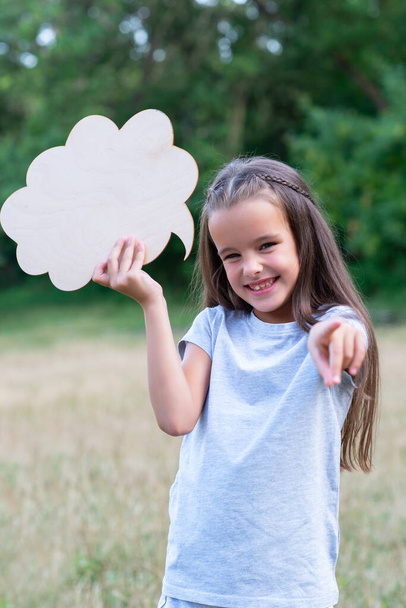 Pretty happy smiling thinking little girl pointing with her finger at camera, summer nature outdoor with cloud of thoughts (like in comic book). Kid's portrait. Emotions, feeling and thoughts of child - 写真・画像