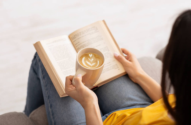 Blijf thuis tijdverdrijf. Onherkenbare vrouw genieten van hete koffie en het lezen van spannende boek, binnen - Foto, afbeelding