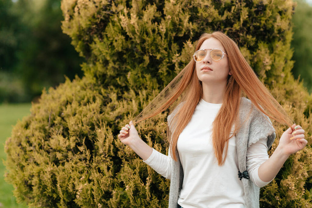 Woman with red hair in orange glasses strokes her hair - Photo, Image