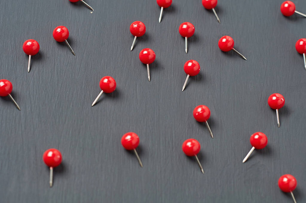 Scattered many red push pins on dark concrete desk in office, school or home. Close-up - Fotografie, Obrázek